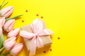 Beautiful tulips with gift box on colored background
