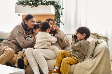 A happy family gathers in living room, sharing laughter and warmth while boy taking photo during the winter holiday season.
