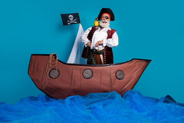 Naklejka premium Photo of positive funny man pirate medieval history hero swim boat isolated on blue color background