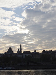 Fototapeta premium Sunset Over River with City Silhouette Against Cloudy Sky
