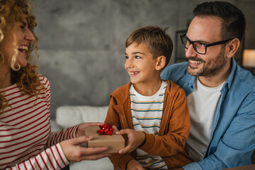 mother and father sit on sofa and give to son special gift