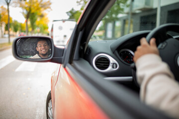 Man smiling in car rear-view mirror while driving in city