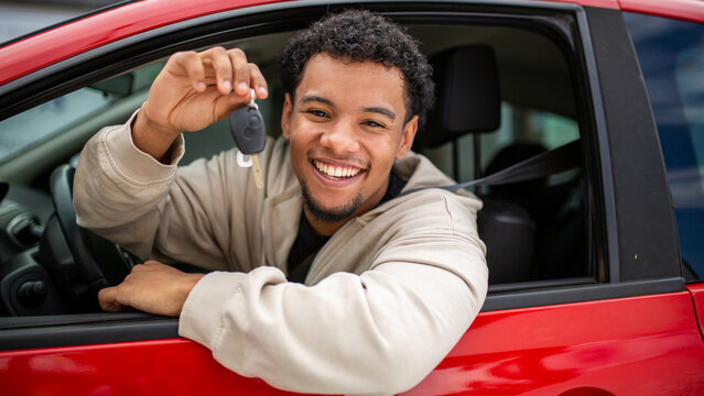 Smiling young man holding car key in red car window