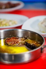 Saucepan with olive oil, garlic and red pepper over a red cutting board with different plates at background