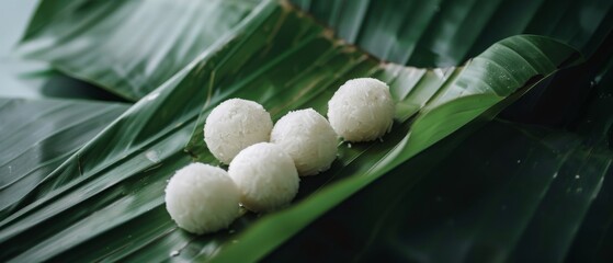 A cluster of white coconut balls rests elegantly on vibrant green banana leaves, capturing a minimalist yet exotic essence.