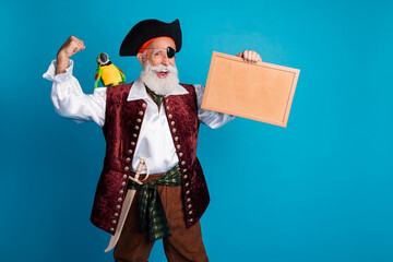 Photo portrait of senior funny pirate grandpa winning hold picture frame wear masquerade party costume isolated blue color background