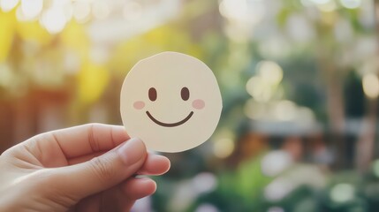 A hand holds a smiling face sticker against a blurred green background.