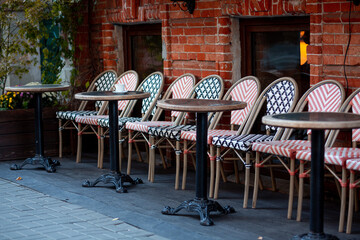 Obraz premium Multi-colored beautiful wicker chairs stand on a city street along the brick wall of a restaurant on a background of wooden round tables