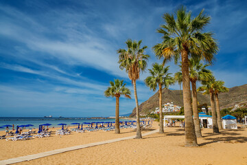 The serene Las Teresitas beach, framed by golden sands, calm blue waters, and tropical palms with mountains rising in the background