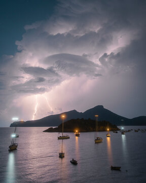 View of dramatic storm with lightning strike over boats and the island of Dragonera, Sant Elm, Spain.