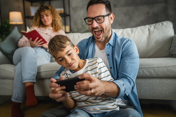 dad and son and play video games on cellphone with mum behind