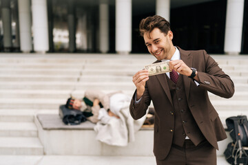 Portrait of laughing businessman in suit smiling looking at camera as holding dollar bill while...