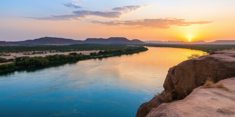 Fototapeta premium A beautiful sunset over a river with a rocky shoreline. The water is calm and the sky is filled with warm colors