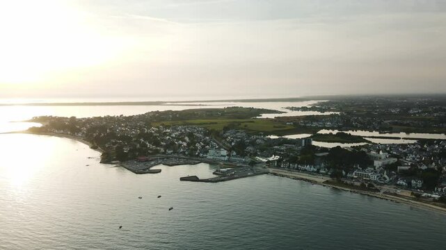 Aerial view of Carnac, Brittany, showcasing its coastal port, seaside homes, and expansive wetlands in soft morning light, capturing the charm of the French coastline.