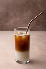 Coffee with coconut milk and ice cubes in a tall glass. Traditional non-alcoholic cold drink. In the background, a jar of coffee and a jar of sugar. Selective focus, close-up.