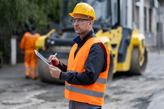 Construction worker assessing road conditions while wearing safety gear at a job site in broad daylight