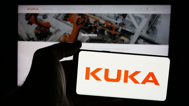 Stuttgart, Germany - 10-24-2024: Person holding mobile phone with logo of German industrial automation company Kuka AG on screen in front of web page. Focus on phone display.