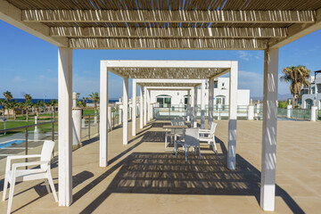 Relaxing terrace view overlooking the ocean with stylish seating and palm trees under a sunny sky.