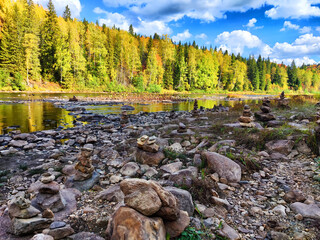 Autumn landscape of a tranquil riverbank with stacked stones under a vibrant blue sky in a forested...