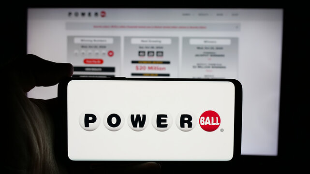 Stuttgart, Germany - 10-24-2024: Person holding cellphone with logo of US lottery game Powerball on screen in front of webpage. Focus on phone display.