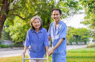 young man caregiver in uniform is taking care of a senior woman while practice walking in the garden