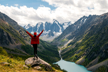 A tourist girl stands on a stone overlooking the beautiful mountains and Lake Shavlinskoye. Altai. Siberia