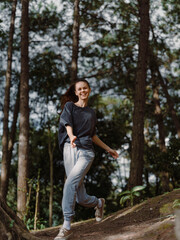 Fototapeta premium Happy young woman running through a forest trail, enjoying nature and outdoor activity with a joyful expression on her face Freedom and adventure concept