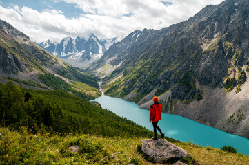 A tourist girl stands on a stone overlooking the beautiful mountains and Lake Shavlinskoye. Altai....