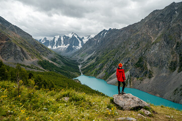 A tourist girl stands on a stone overlooking the beautiful mountains and Lake Shavlinskoye. Altai. Siberia