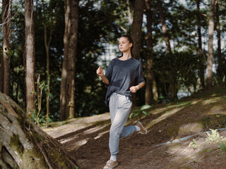 Energetic young woman jogging in a serene forest, wearing casual athletic attire, enjoying nature and fitness Healthy lifestyle and exercise concept