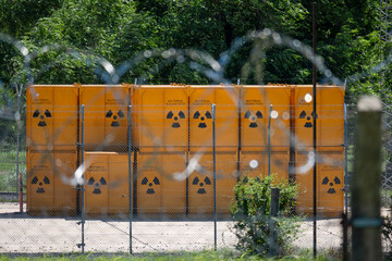 Group of yellow barrels stacked with radioactive waste, behind a ball of barbed wire.