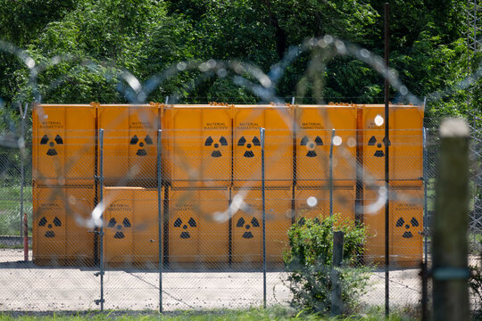 Group of yellow barrels stacked with radioactive waste, behind a ball of barbed wire.