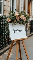 A charming welcome sign with cursive writing and pink roses invites guests at a grand English mansion, surrounded by greenery and romantic gardens
