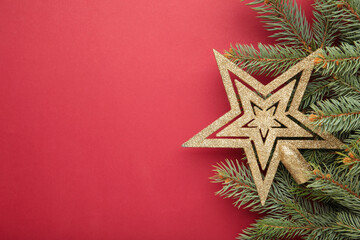 Christmas frame made of fir branches, golden decorative star on red background. Space for text