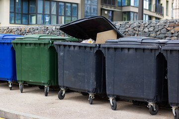 Different colored garbage cans are lined up in front of a building
