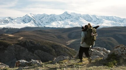 Back view at two hiker women with backpack raising arms for joy, celebrating climbing success standing on high mountain peak at scenic landscape. Travel achievements and recreation together