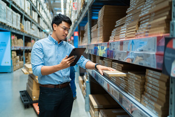A man is looking at a shelf of boxes with a tablet in his hand. He is checking the boxes for a specific item