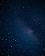 Fototapeta premium A dark night sky filled with a vast expanse of stars, a faint band of the Milky Way stretching across the frame.