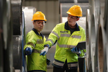 two professional engineer, worker, technician use clipboard discuss work, walk in steel metal manufacture factory plant industry. Asian man and woman wear hard hat check quality machine