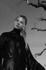 Fototapeta premium Fashion portarait of a young blonde girl in black strange dress. Autumn nature and tree branches. Black and white