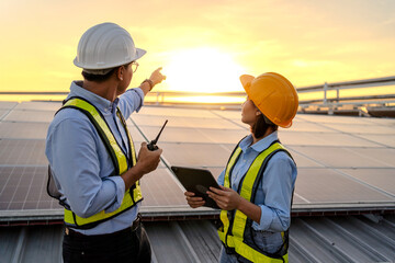 Two construction workers are standing on a roof, one pointing to something on the ground. They are wearing safety gear and holding a tablet