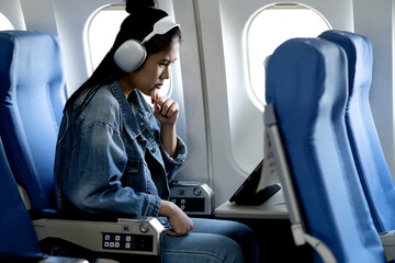 young woman sitting on a plane looking at a tablet for information and entertainment while traveling on an airline  making business and news non-stop even though she is far away 