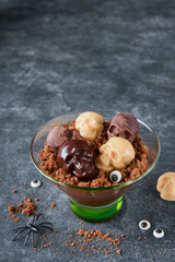 Halloween party chocolate puddings or Panna Cotta with brownie crumbles and chocolate sculls served in clear glass on grey dark background. Party idea for Halloween.