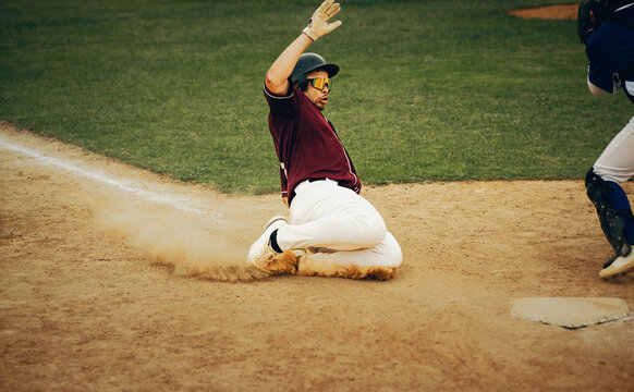 Baseball player slides into home plate, creating a cloud of dust during a competitive game