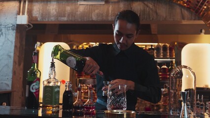 Portrait good looking Asian bartender using jigger measure liquor syrup into mixing glass preparation at luxurious beverage counter bar, neat professional barman costume at nightclub luxury. Vinosity.