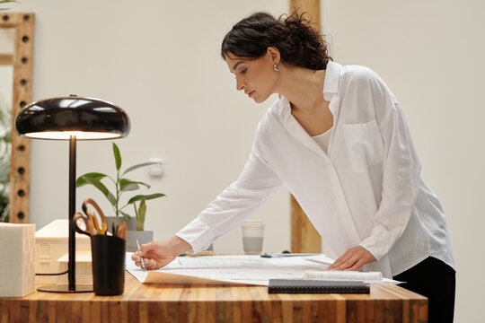 Architect in spacious office carefully examining architectural plan on desk
