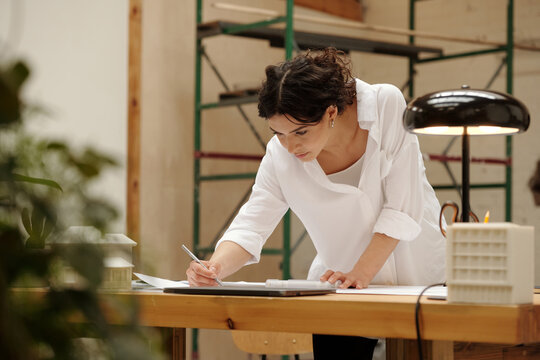 Architect focusing on design project in a well-lit studio space while bending over desk