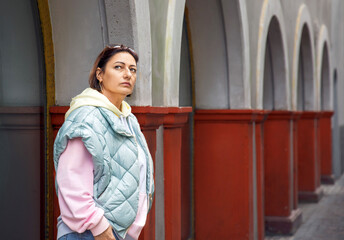 Woman in stylish casual outfit standing by arched building corridor