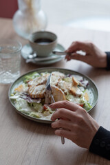Close-up of hands with a plate of Caesar salad near the window in a cafe, during the day.