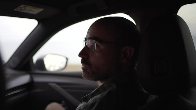 horizontal video of co-driver watching the road, man in his forties, with glasses and bald head.
